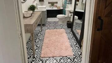 A narrow hallway leading to a bathroom with a white sink, a toilet, and a mirror. The floor has a black and white patterned tile.