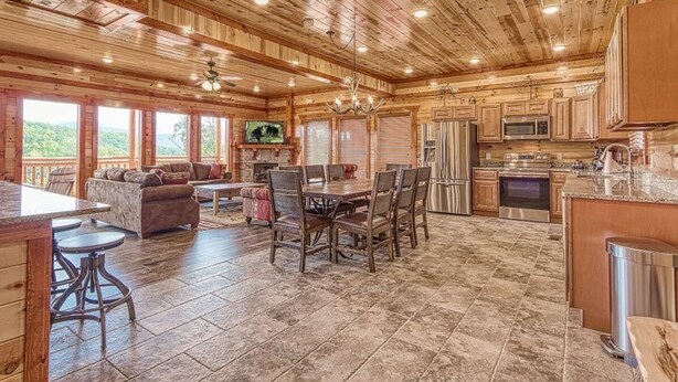 A spacious log cabin interior with a dining area, kitchen, and a fireplace. - *Soaring Eagle* VIEWS! Heated POOL-Theater-Game Rm (Sevierville)