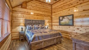 A wooden cabin bedroom with a bed, two bedside tables, a ceiling fan, and a painting on the wall. - *Soaring Eagle* VIEWS! Heated POOL-Theater-Game Rm (Sevierville)