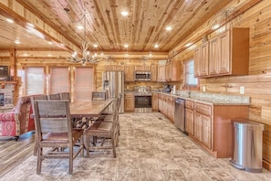 A log cabin interior with a dining area, kitchen, and a fireplace.