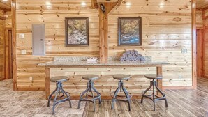 A wooden cabin interior with a bar area featuring four stools and two framed pictures on the wall. - *Soaring Eagle* VIEWS! Heated POOL-Theater-Game Rm (Sevierville)