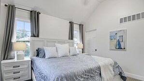 A bedroom with a bed, nightstands, a window with curtains, and a painting on the wall.