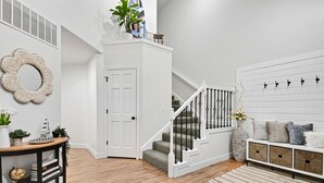 A modern interior with a staircase, a white console table, and a seating area with cushions.