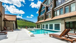 A modern hotel with a pool area, lounge chairs, and a mountain view.