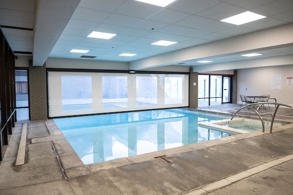 Una piscina interior con paredes de vidrio transparente, suelo de baldosas y escalera metálica.