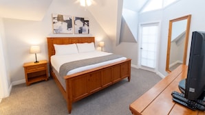 A bedroom with a wooden bed, bedside tables with lamps, a ceiling fan, and a TV on a wooden stand.