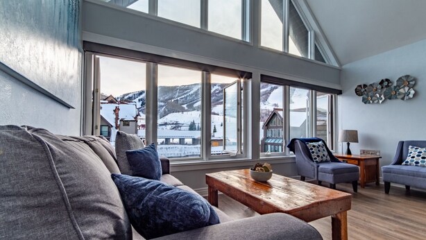 A spacious living room with a large window offering a view of a snowy mountain landscape.