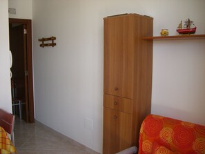 A room with a wooden wardrobe, a small shelf with decorative items, a patterned sofa, and a door leading to another room. - Dimora Liccisa Attic in Torre Lapillo-porto Cesareo-punta Prosciutto (Nardò)