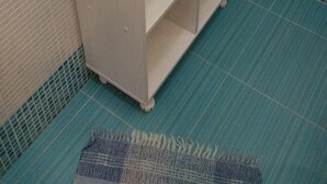 Un portasciugamani bianco con asciugamani piegati e un cesto in vimini in un bagno con pareti piastrellate in blu e bianco.