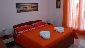 Una camera d'albergo con un letto, cuscini, un comodino, una lampada, un quadro appeso al muro e una finestra con tende.