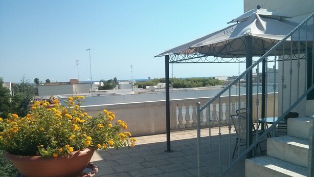 Una terrazza con una pianta in vaso, un'area salotto coperta e una scala che conduce a un livello superiore.