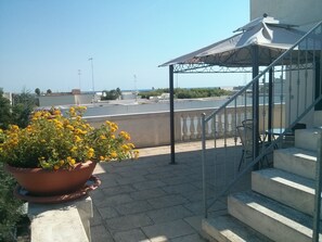 Une terrasse agrémentée de plantes en pot, un espace salon couvert et un escalier menant à un niveau supérieur.