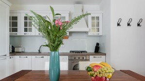 A kitchen with white cabinets, a teal vase with flowers, and a fruit bowl on the table. - Villa Athos 2 With two Apartments, Pool and Garden (Labin)