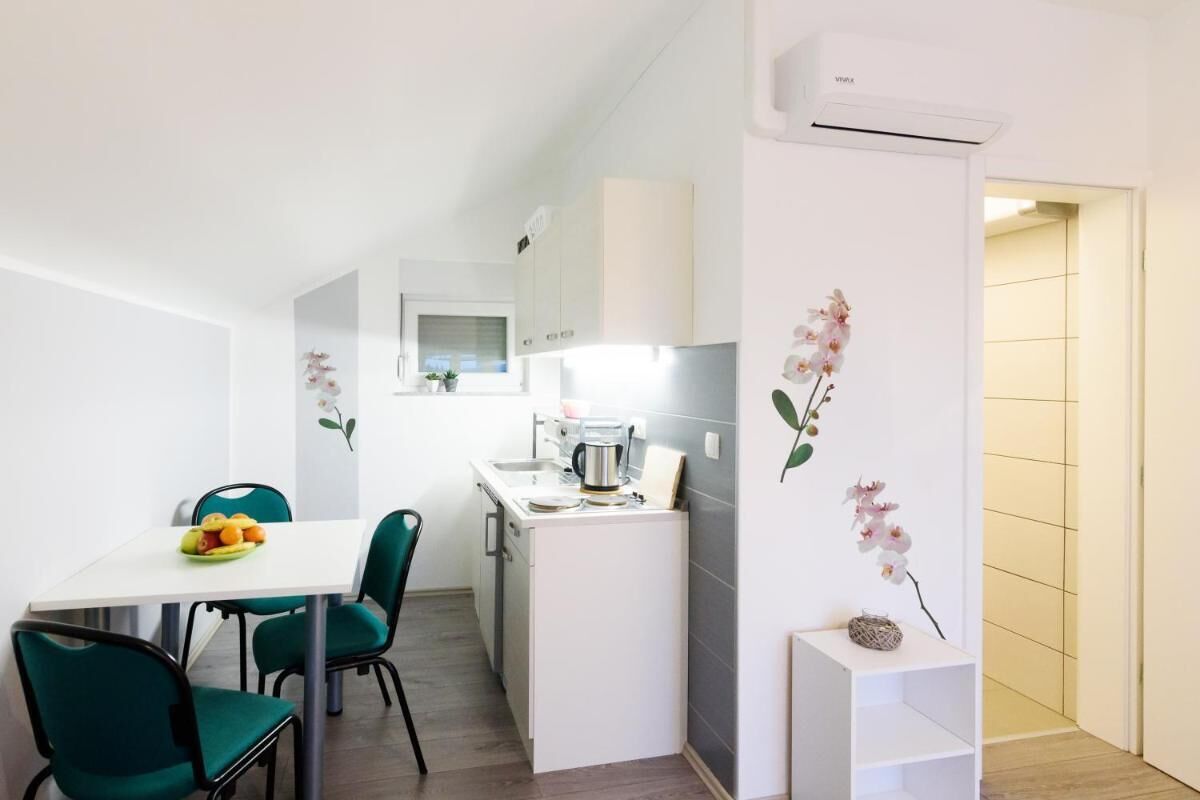 Een compacte keuken met witte kasten, een koffieapparaat en een klein eiland. Er is een eethoek met een witte tafel en groene stoelen.