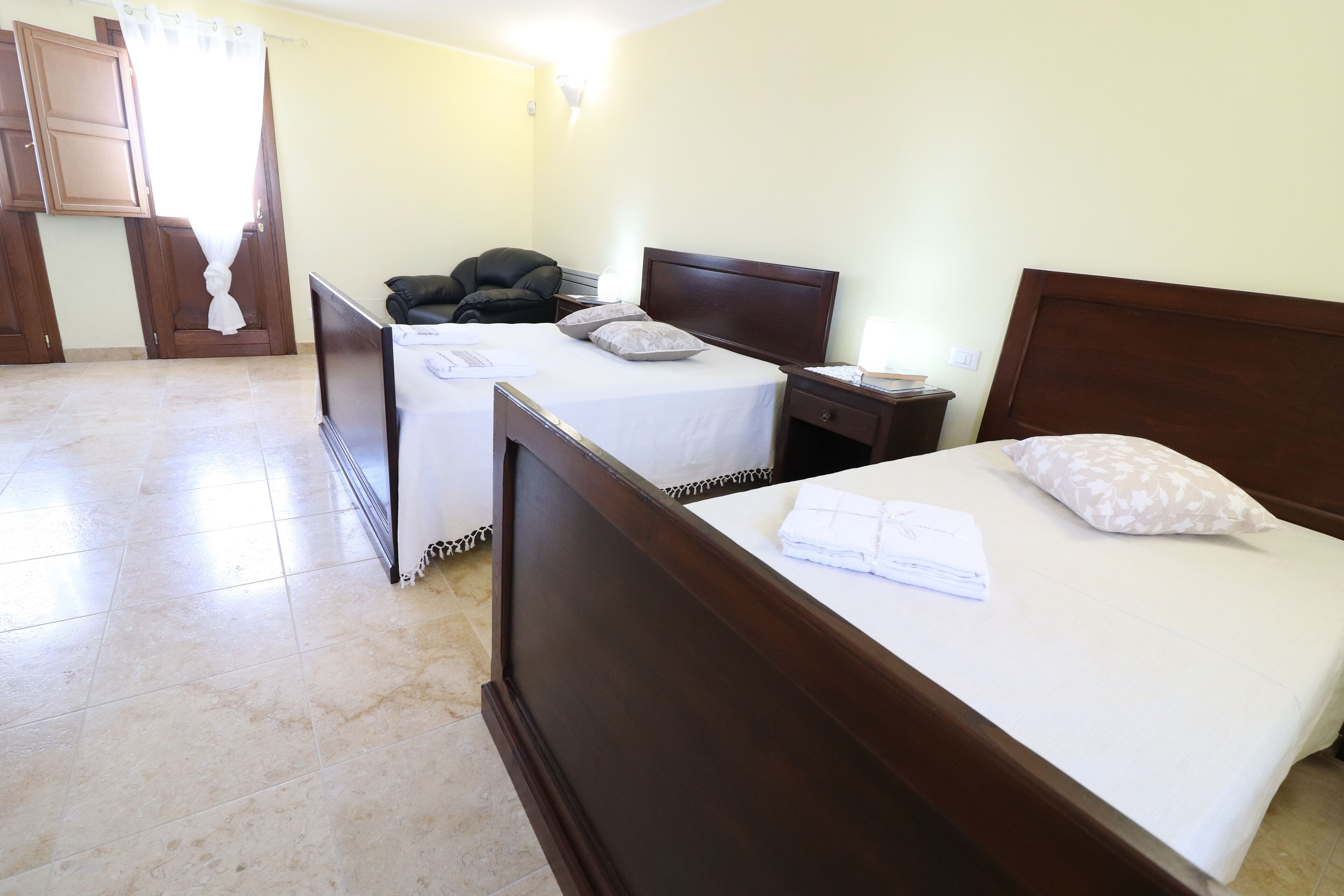 A hotel room with two beds, a chair, a nightstand, and a window with curtains.