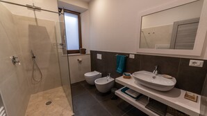 Une salle de bain moderne avec une douche à parois de verre, deux bidet, un grand lavabo et un miroir au-dessus du lavabo.
