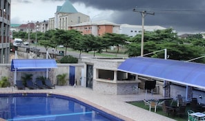 A swimming pool with lounge chairs, a covered outdoor seating area, and a building with a dome roof in the background.