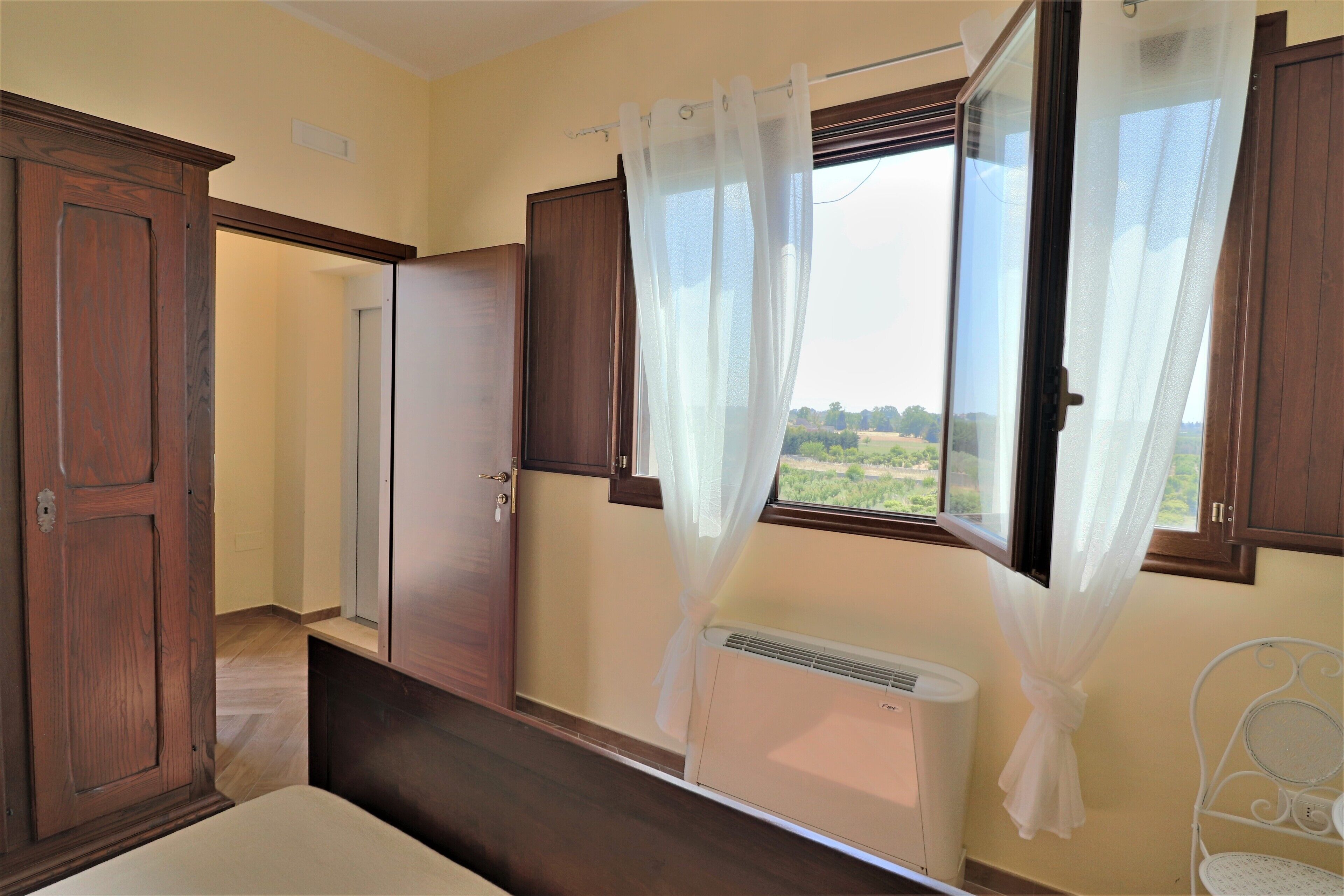 A bedroom with a large window, a radiator, and wooden furniture.