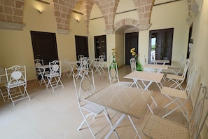 A spacious indoor area with multiple white metal tables and chairs arranged in a semi-circular pattern, surrounded by brick arches and large windows. - Comfort Lime Double (Carmiano)