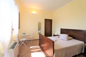 A bedroom with a bed, a chair, a small table, a mirror, and a door. - Comfort Lime Double (Carmiano)