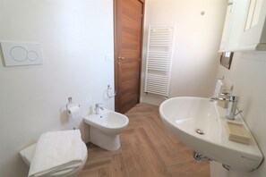 A bathroom with a bidet, a sink, a towel, and a wooden door. - Triple Comfort Pink Grapefruit (Carmiano)