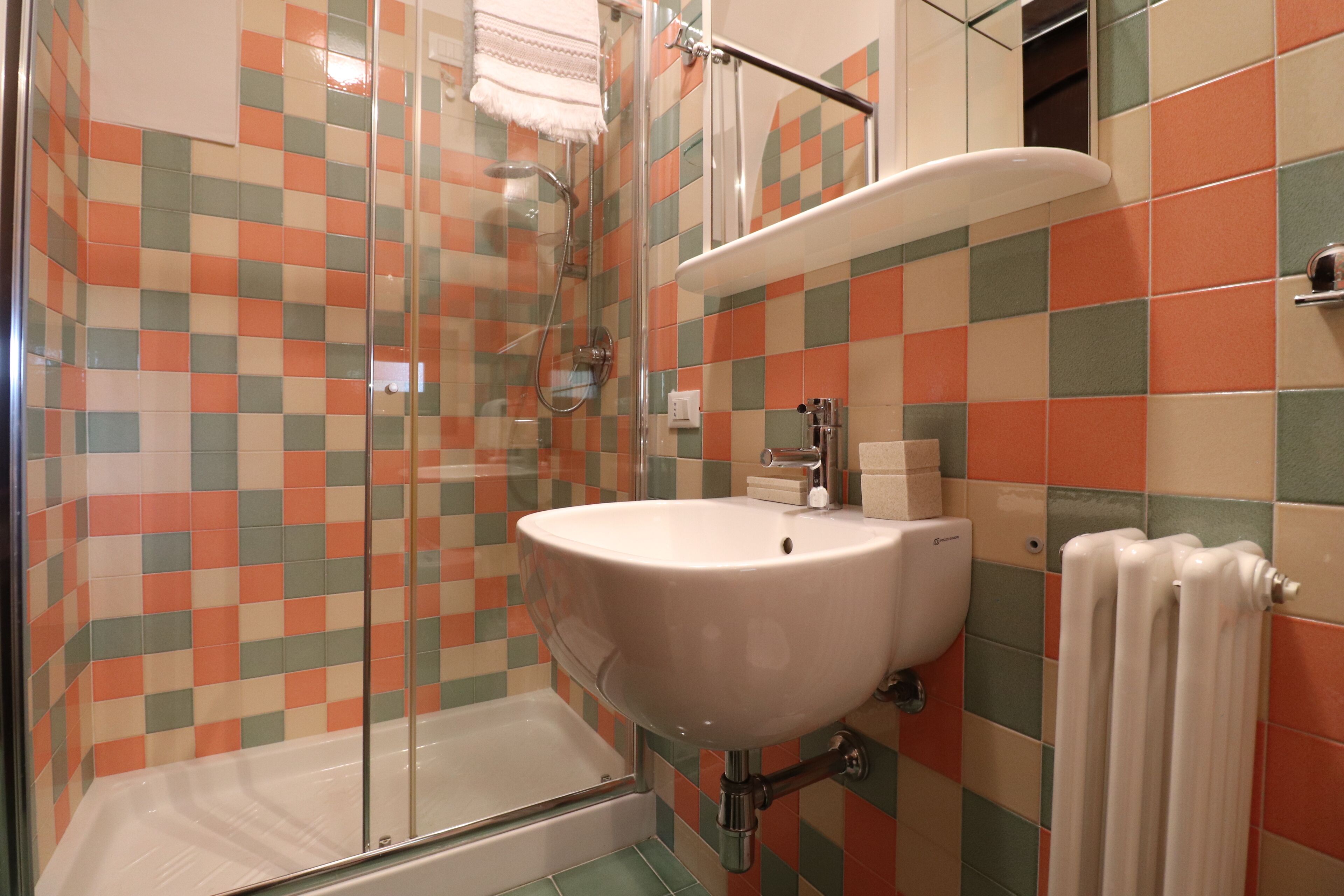 A bathroom with a checkered tile pattern, a white sink, a glass shower enclosure, and a white towel hanging on a radiator.