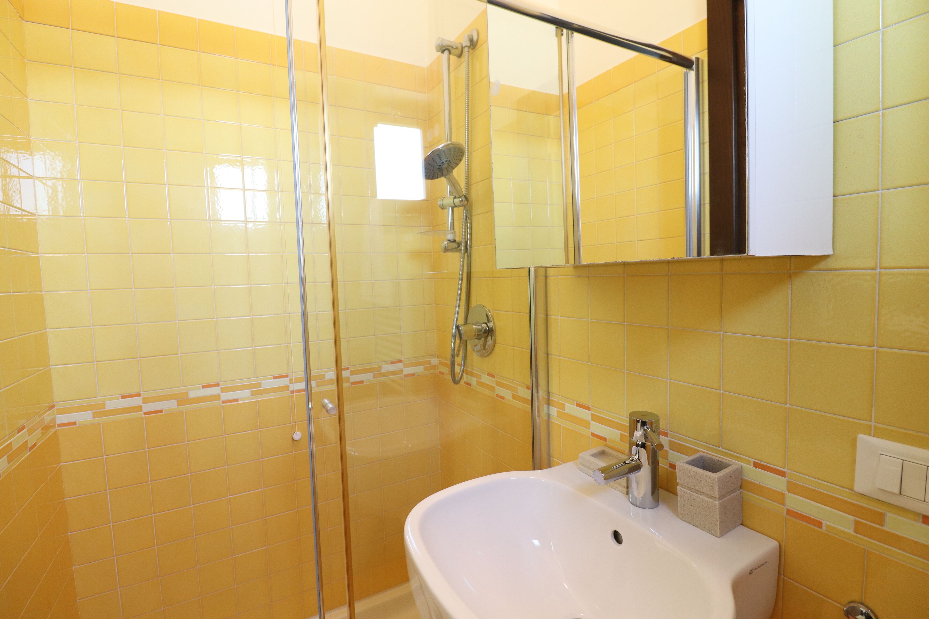A bathroom with yellow tiles, a glass shower enclosure, a white sink, and a mirror above it.