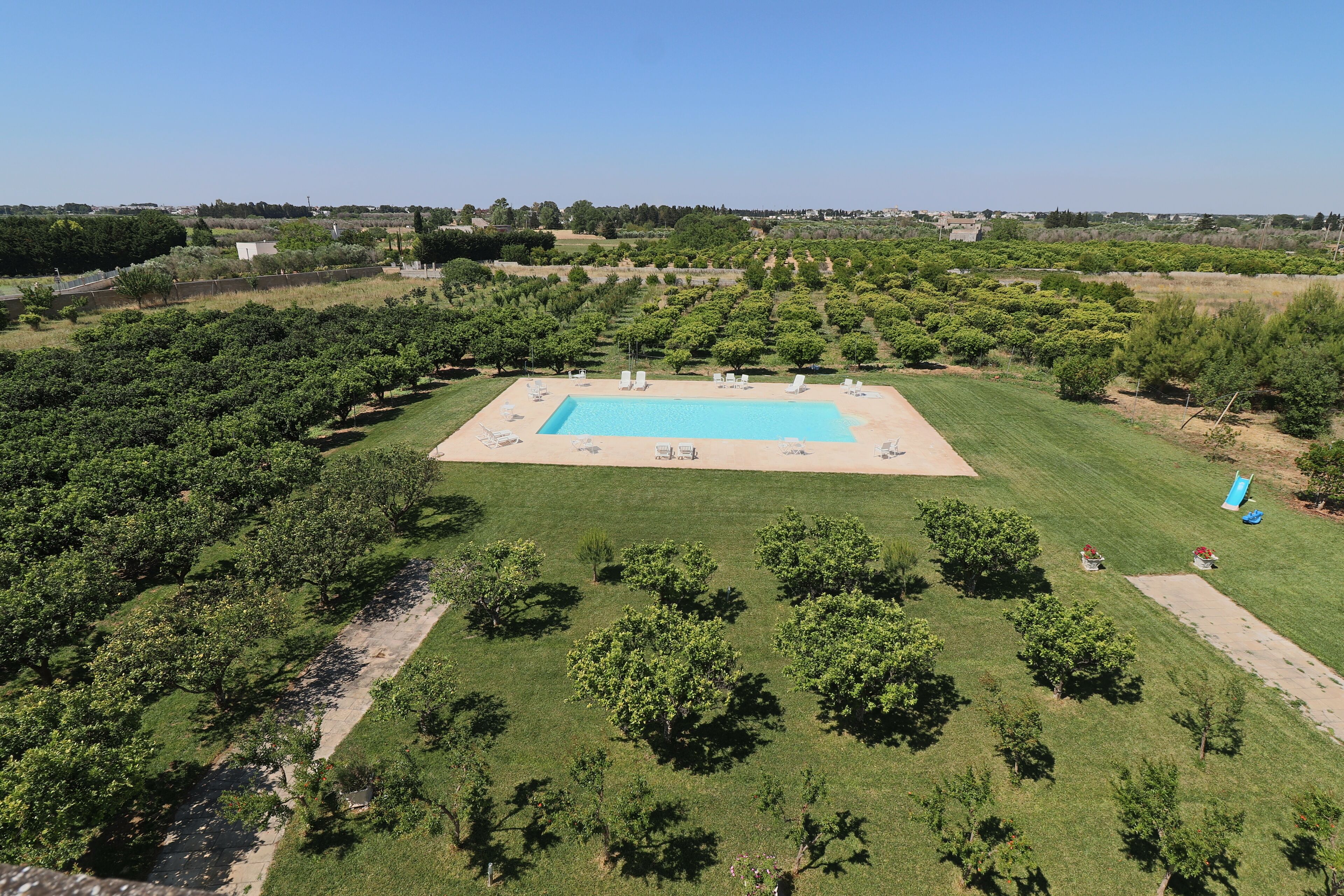 An aerial view of a property with a swimming pool surrounded by a well-maintained lawn and trees.