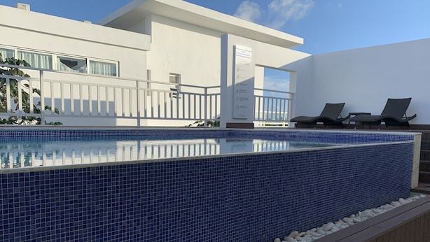 A modern pool area with a blue-tiled edge, a wooden deck, and lounge chairs. - Peace In The Village, Punta Cana Village (Punta Cana)
