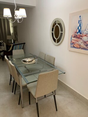 Een eetruimte met een tafel met glazen blad, beige stoelen en een decoratieve kom.