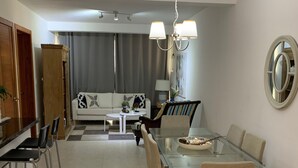A modern dining area with a glass table, metal chairs, and a sofa in the background. - Peace In The Village, Punta Cana Village (Punta Cana)