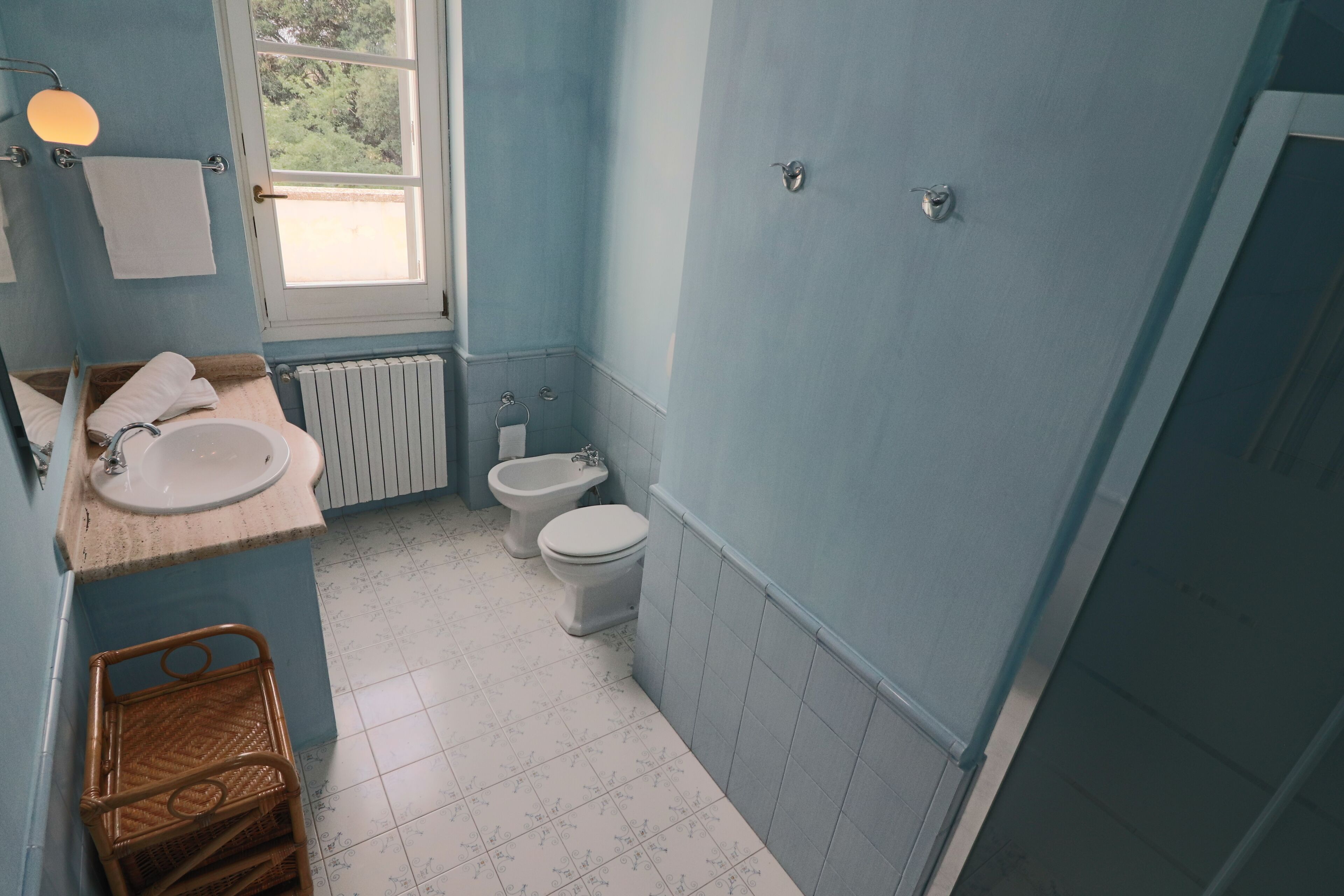 A bathroom with a sink, toilet, and bidet, featuring blue walls and white tiled floors.