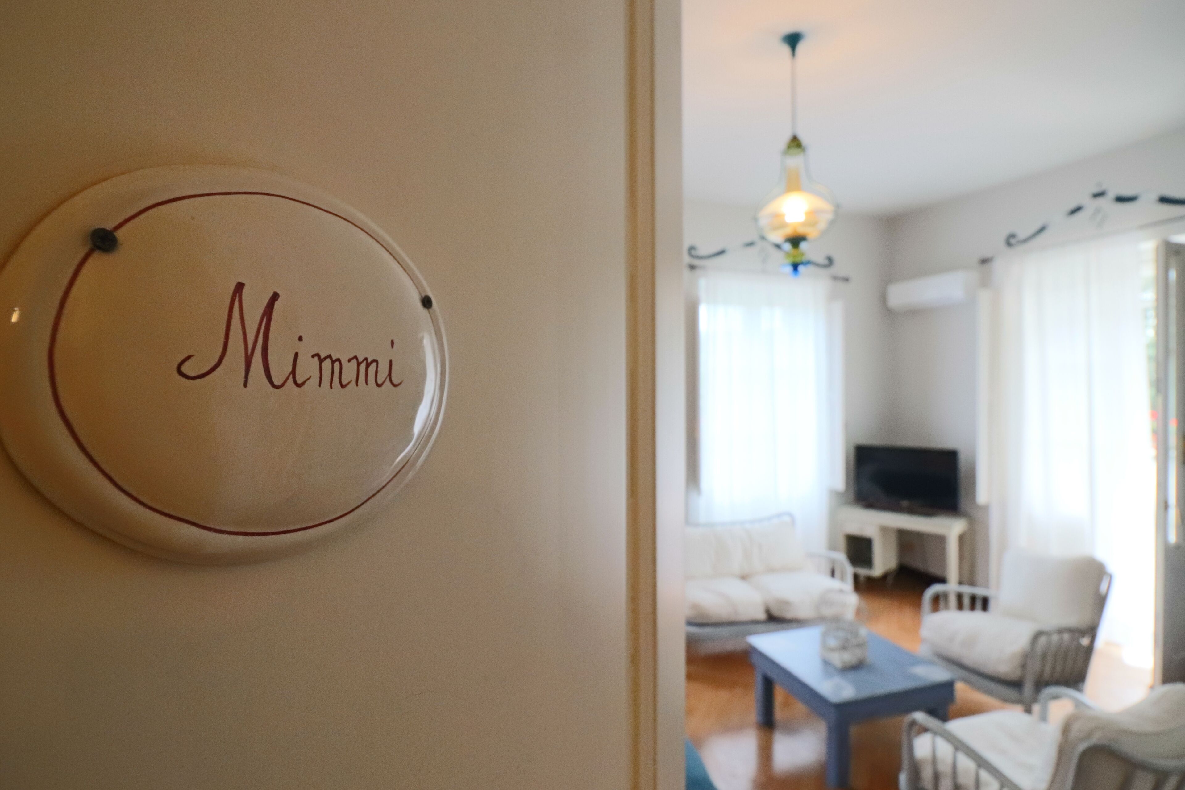 A room with a sign reading "Mimmi" on the wall, a television, and a seating area with a table and chairs.