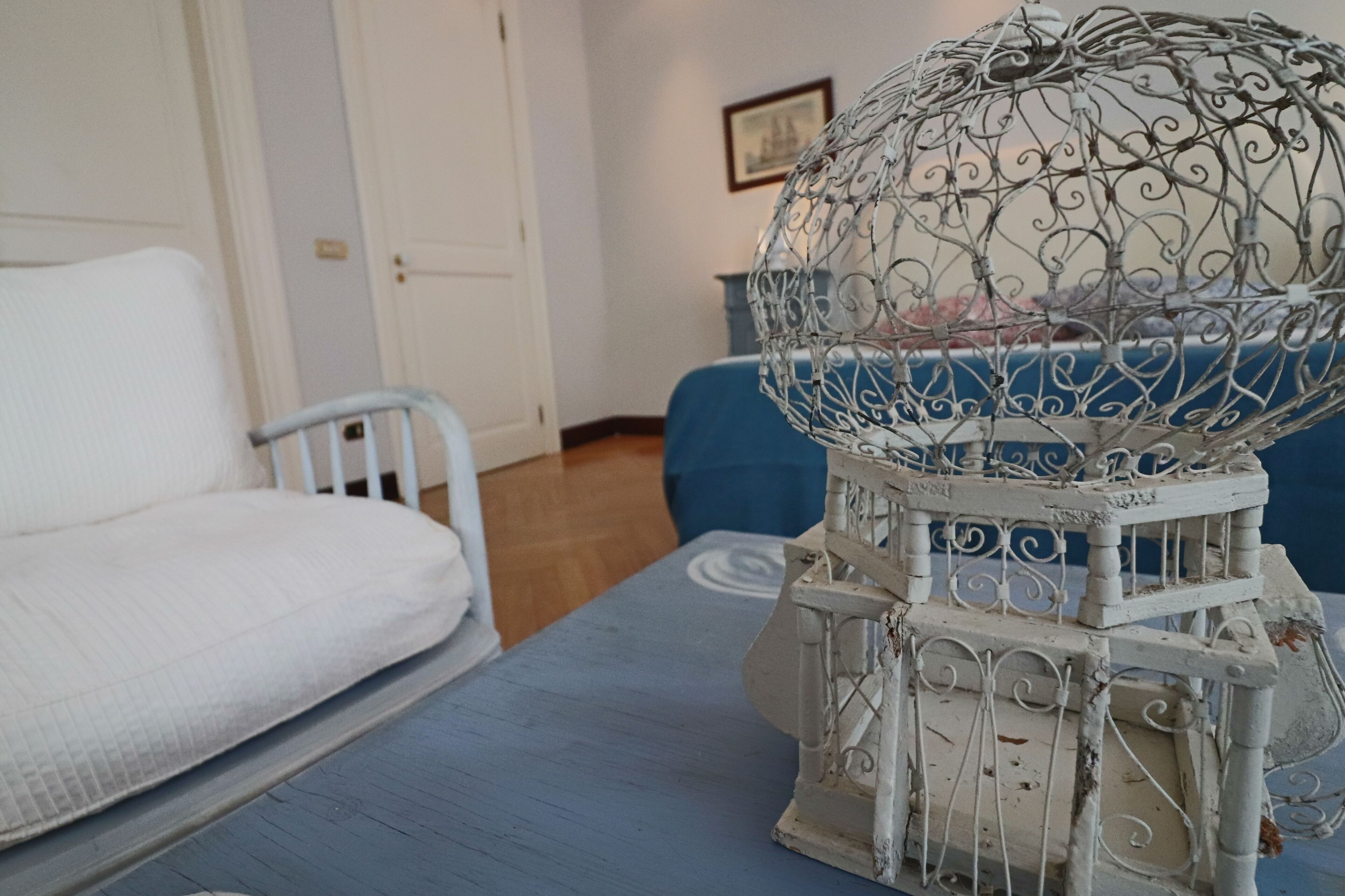 A white metal sculpture on a table, a white chair, and a blue sofa in a room with wooden flooring and white walls.