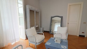A room with a wooden floor, two white chairs, a blue table with decorative items, a wardrobe, and a mirror. - Relais Delle Rose - Mimmi Executive Suite (Lecce)