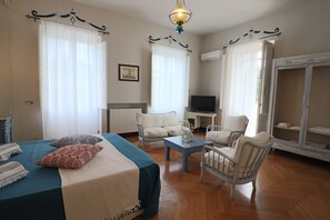A well-lit room with a bed, two armchairs, a small table, and a television.