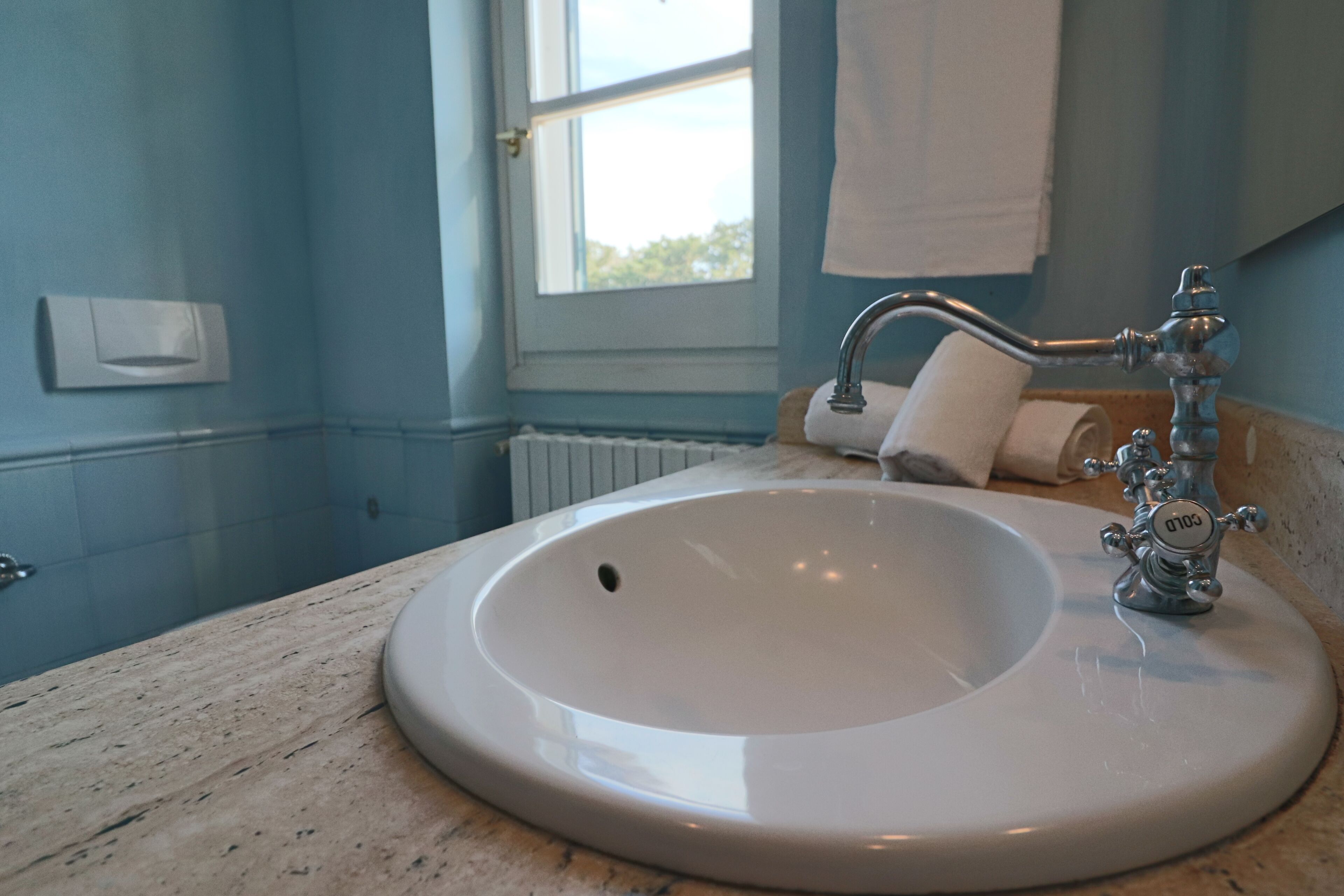 A bathroom with a white sink, a window with a view, and a towel rack.