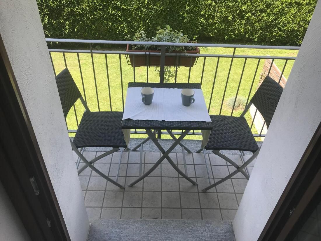 Een balkon met een tafel en twee stoelen, een bloempot en uitzicht op een groen gazon.