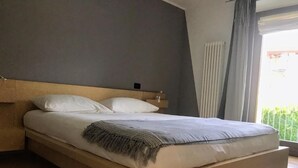 Ein modernes Schlafzimmer mit einem Holzbettgestell, einer grauen Kopfstütze und Blick auf Grünfläche.