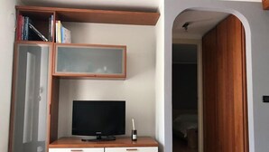 Ein Zimmer mit Fernseher auf einer Holzkommode, einem Bücherregal und einem Kleiderschrank.