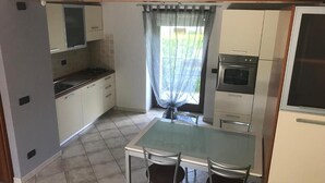 Eine kleine Küche mit Esstisch und Stühlen, einem Fenster mit Vorhängen und einem Kühlschrank.