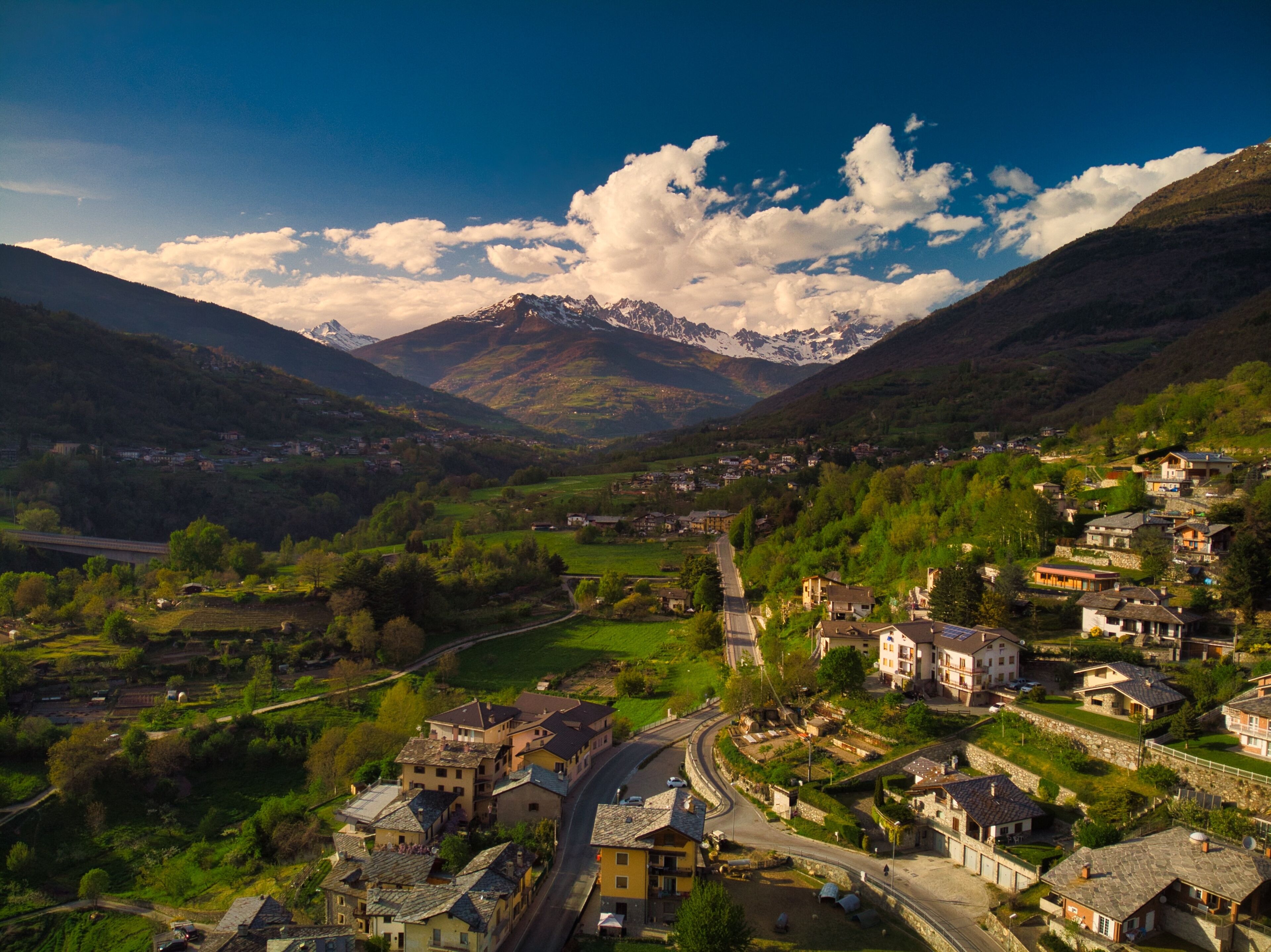 Un village de montagne aux bâtiments traditionnels, avec une route sinueuse et une vallée.