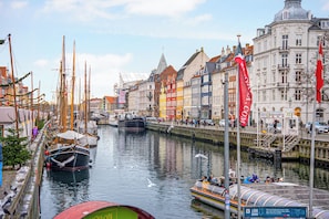 Um canal ladeado por edifícios coloridos e barcos, com vista para a água e uma ponte ao fundo.