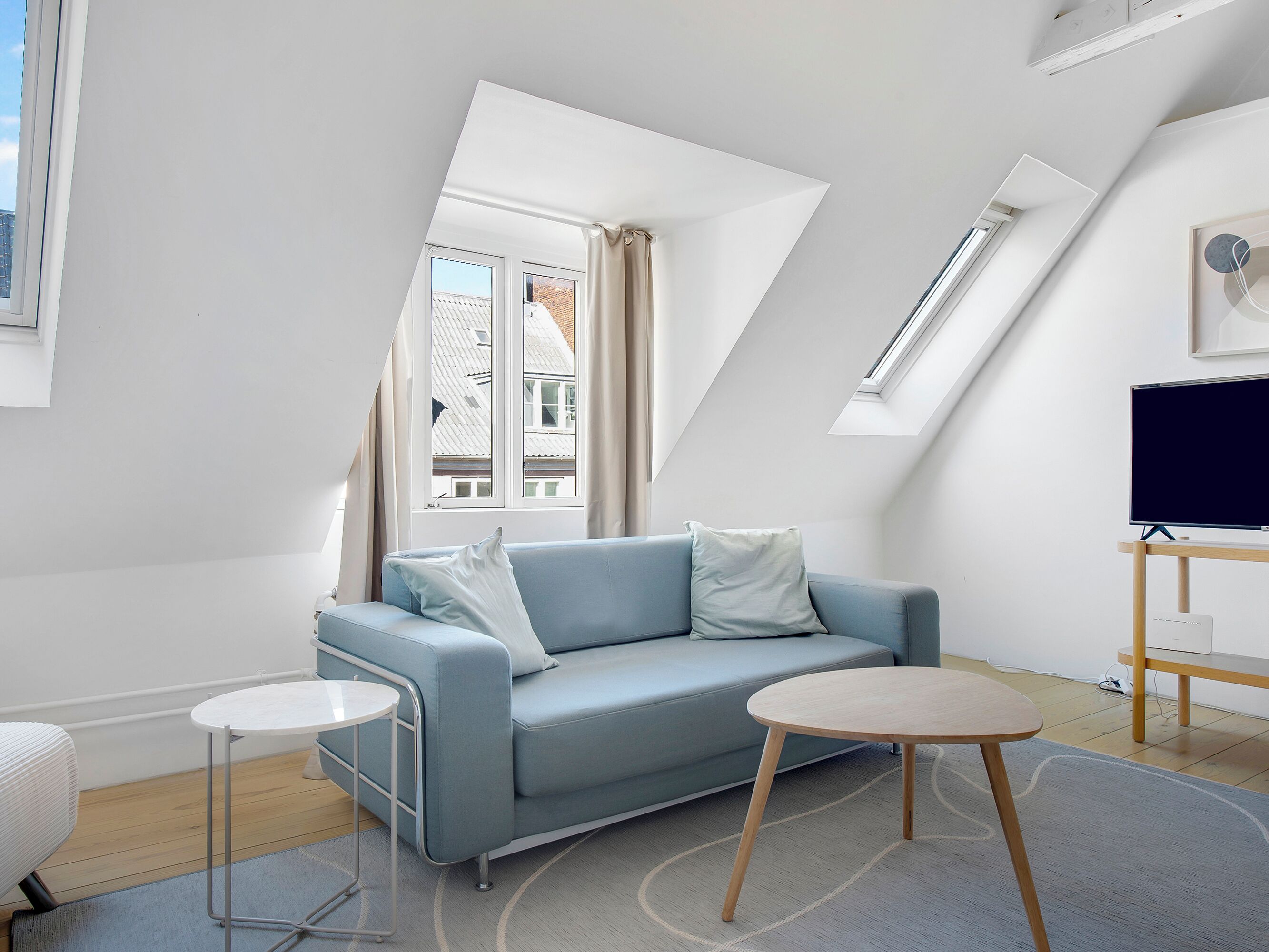 Un salon moderne avec un canapé bleu clair, une petite table ronde et un téléviseur posé sur un meuble en bois.