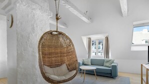 Een moderne woonkamer met een hangstoel, een bank, een klein tafeltje en uitzicht op de stad door een raam.