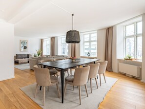 A modern living room with a dining area, large windows, and a hanging light fixture.