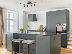 A modern kitchen with a central island, bar stools, a built-in oven, and a large window.