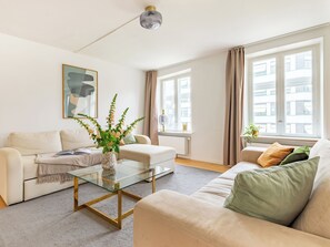 A modern living room with a glass coffee table, beige sofas, a vase with flowers, and large windows with curtains.