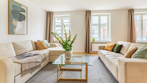 A modern living room with two sofas, a glass coffee table, a vase with flowers, and a framed abstract painting. - Regent 7 - Large 3 Bdr Apt With Balcony in City Centre (Copenhagen)
