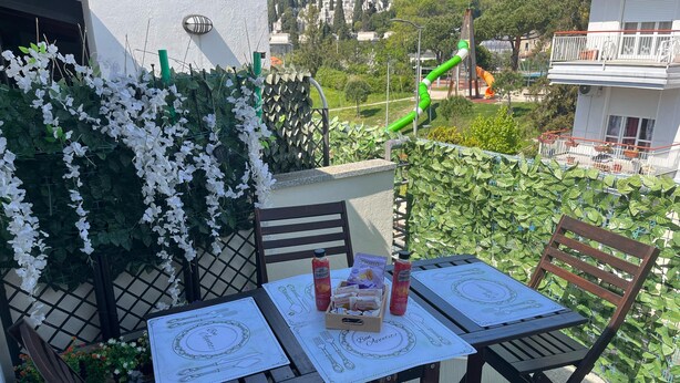 Een balkon met een tafel voor twee personen, omringd door groen en met uitzicht op een speeltuin.
